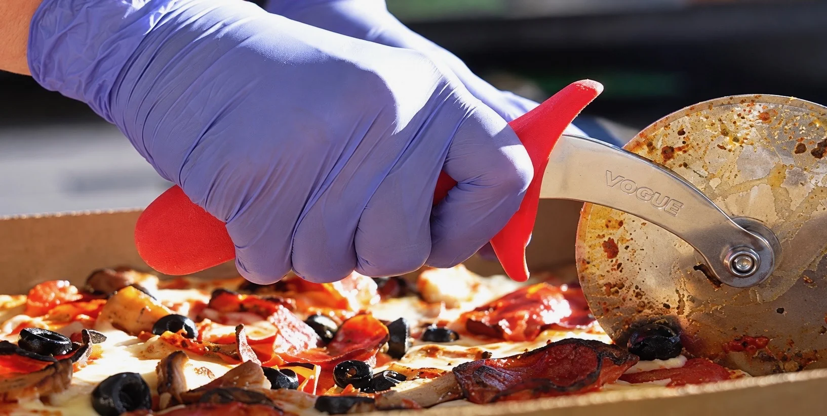 A gloved hand slicing a freshly prepared pizza with a pizza wheel